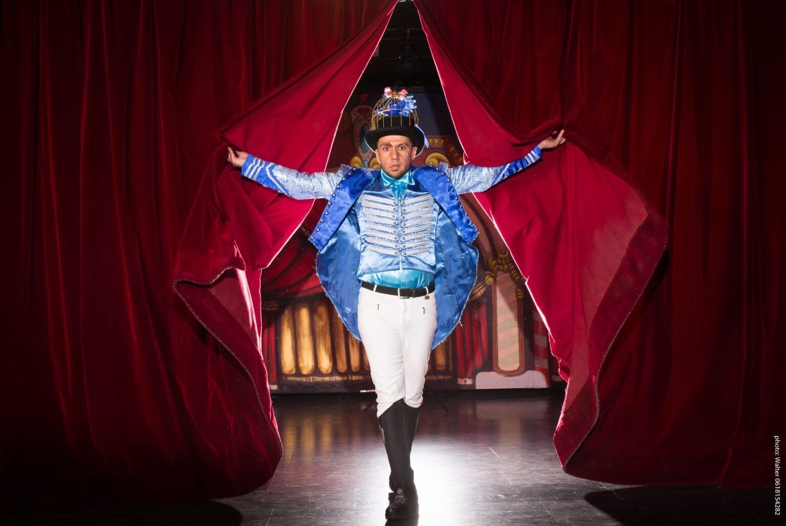 Danseur en costume bleu qui rentre sur scene qui ouvre les rideaux rouges