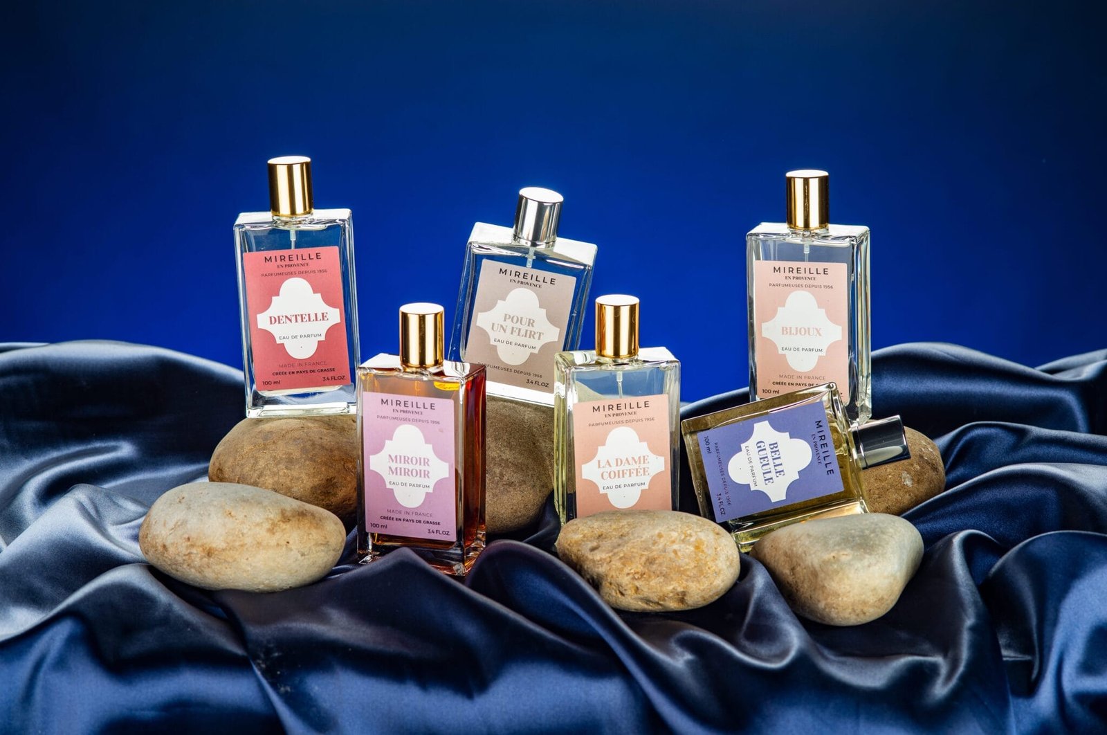 Composition publicitaire avec fond bleu et de six flacons de parfum avec des galets de riviere et du tissu satiné bleu